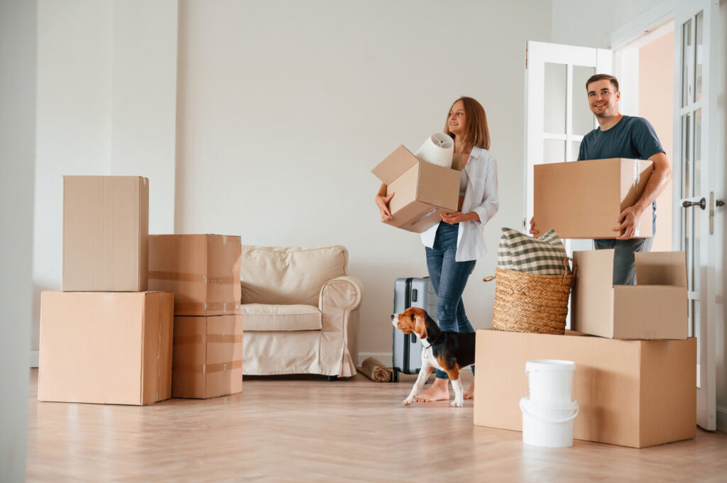 Walking forward with boxes. Young couple with dog are moving to new home.