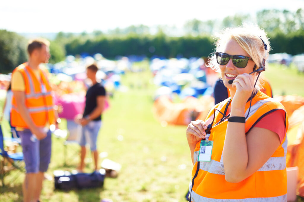 Festival security, communication and a woman outdoor on a grass field for safety at a music concert. Party, event and crowd control with a female officer using a headset microphone for protection.