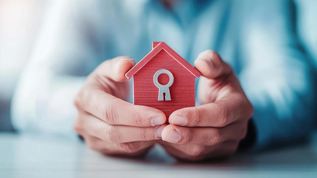 A person holds a small red house model with a keyhole, symbolizing home ownership and security in real estate.